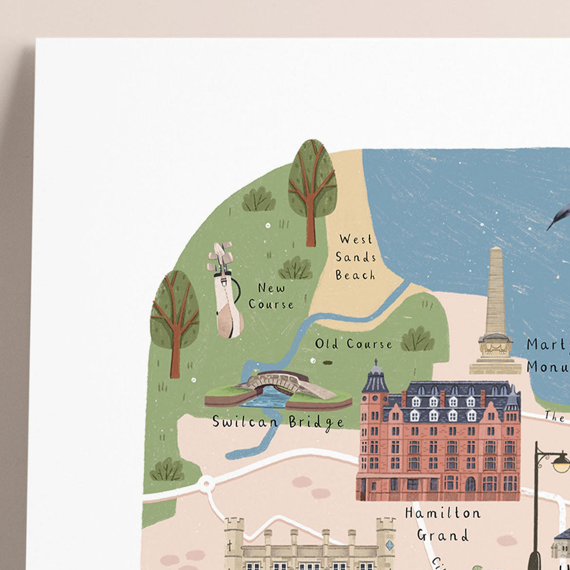 A close-up of an illustrated map print of St Andrews, showing the golf course and local landmarks, including West Sands Beach, Swilcan Bridge, Hamilton Grand, and Martyr's monument, with a white border around the artwork.