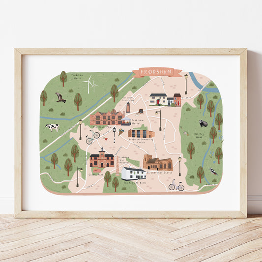 An illustrated map print of Frodsham showing local landmarks, trees, paths, and small drawings of animals, displayed in a wooden frame against a light wall on a wood floor.